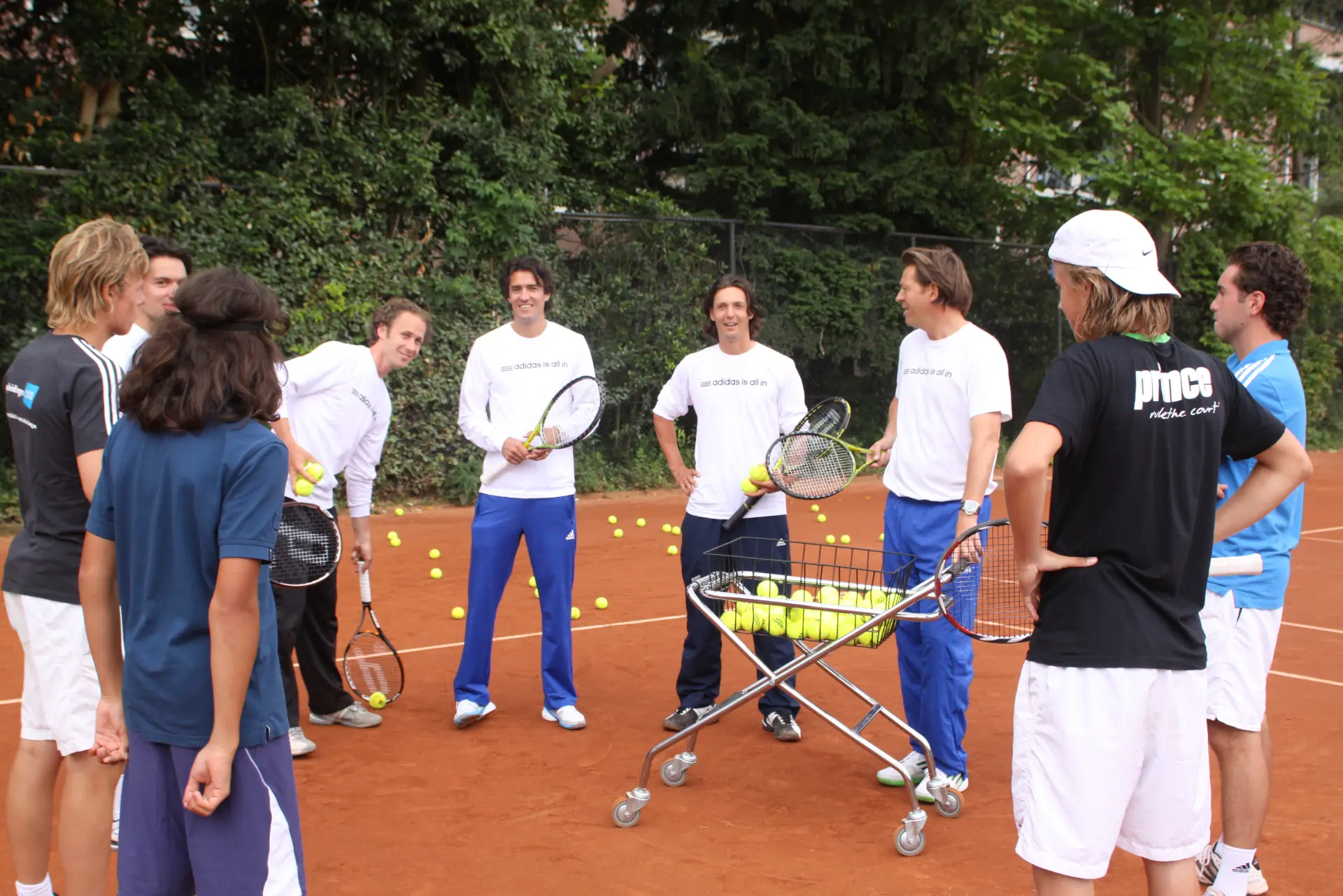 Coaches en spelers van Tennis Academy Amsterdam in een kring rond een ballenkar tijdens een training op gravel, 2011.