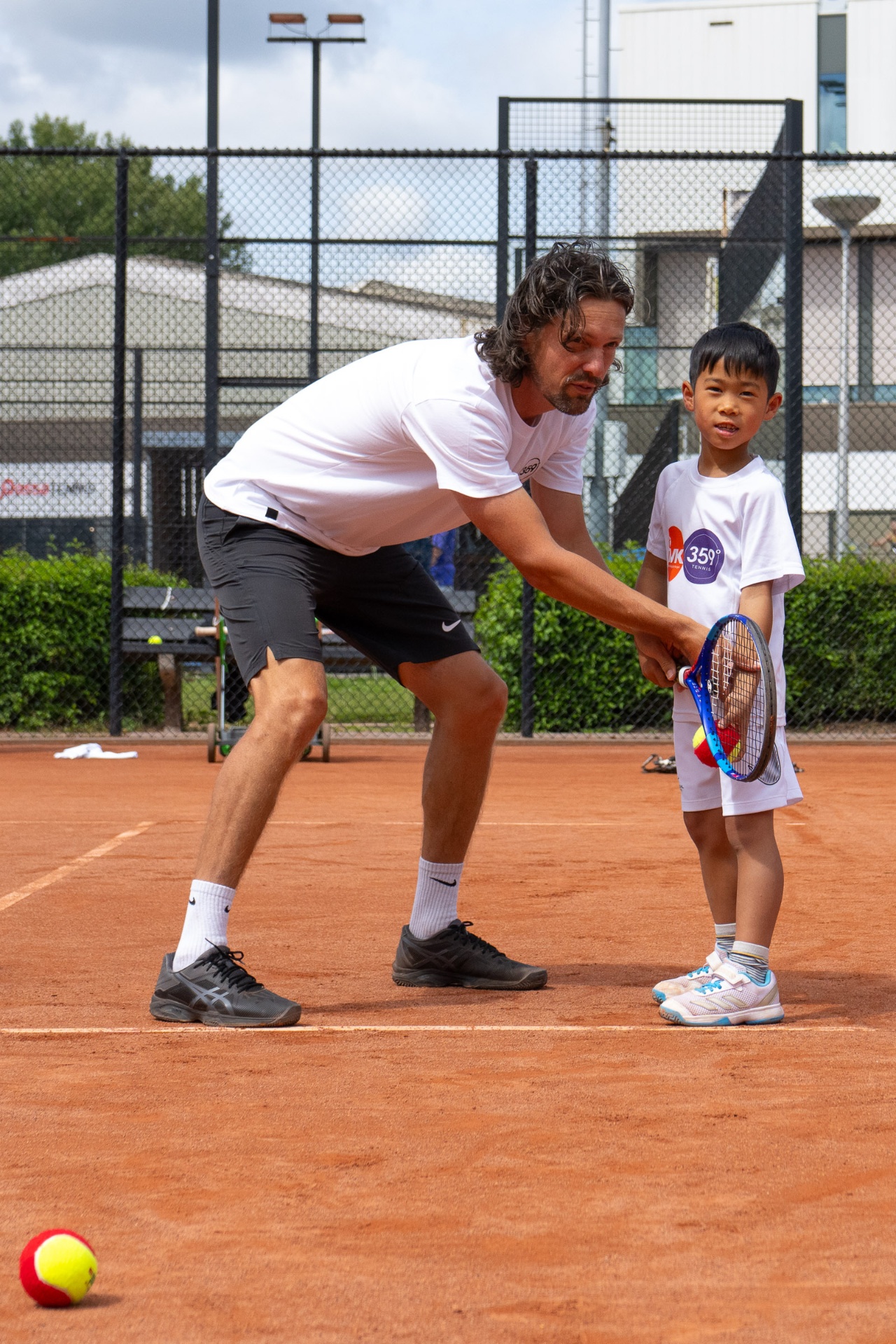 359-coach corrigeert de forehand-grip van een jong Tenniskids-lid tijdens een privéles op de gravelbaan