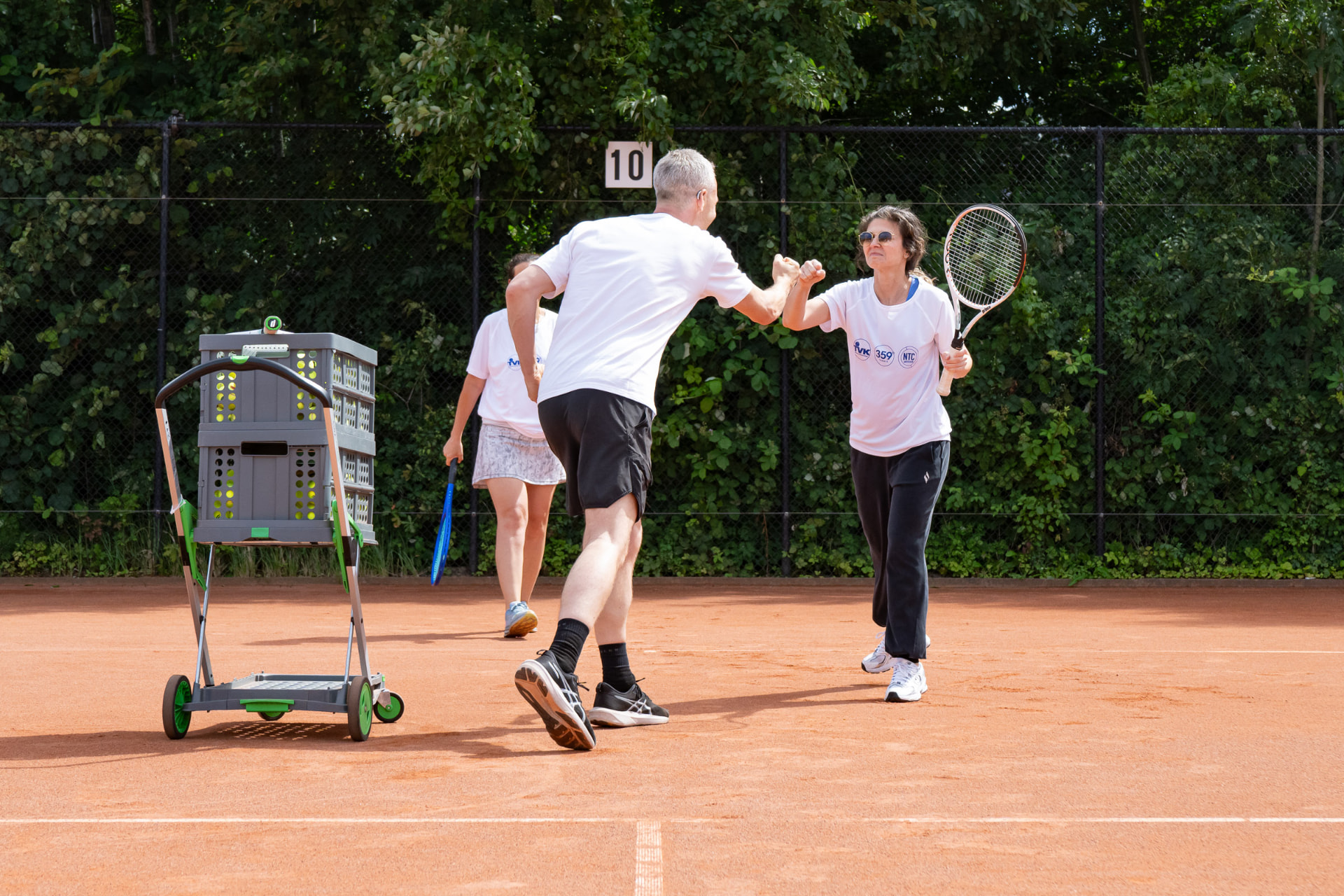 Twee volwassen spelers geven elkaar een fistbump tijdens tennisles op gravel — 359.tennis