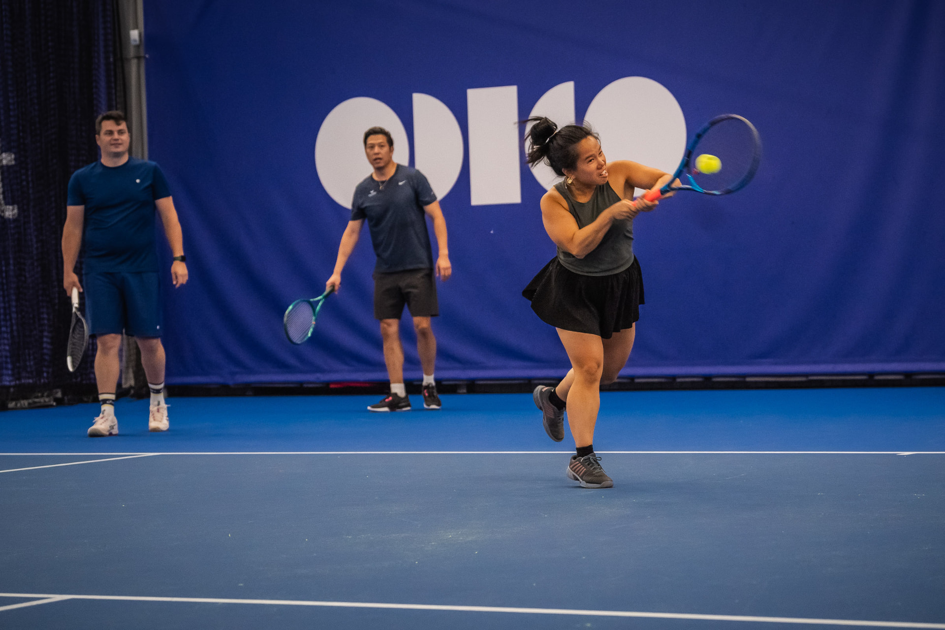 Volwassen speelster slaat backhand tijdens groepsles indoor — 359.tennis