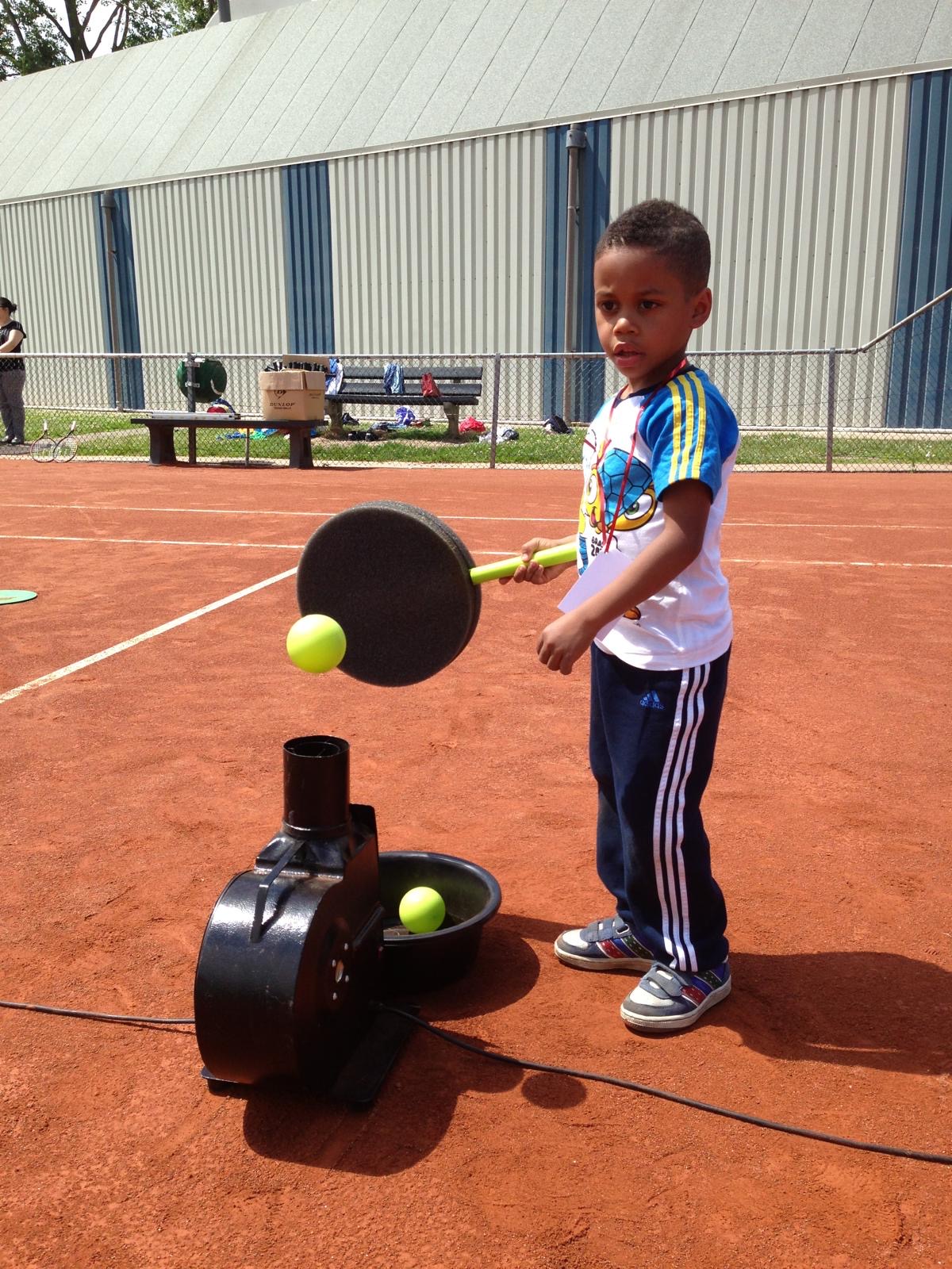 Young child hitting a floating ball with a foam floater racket on a clay court