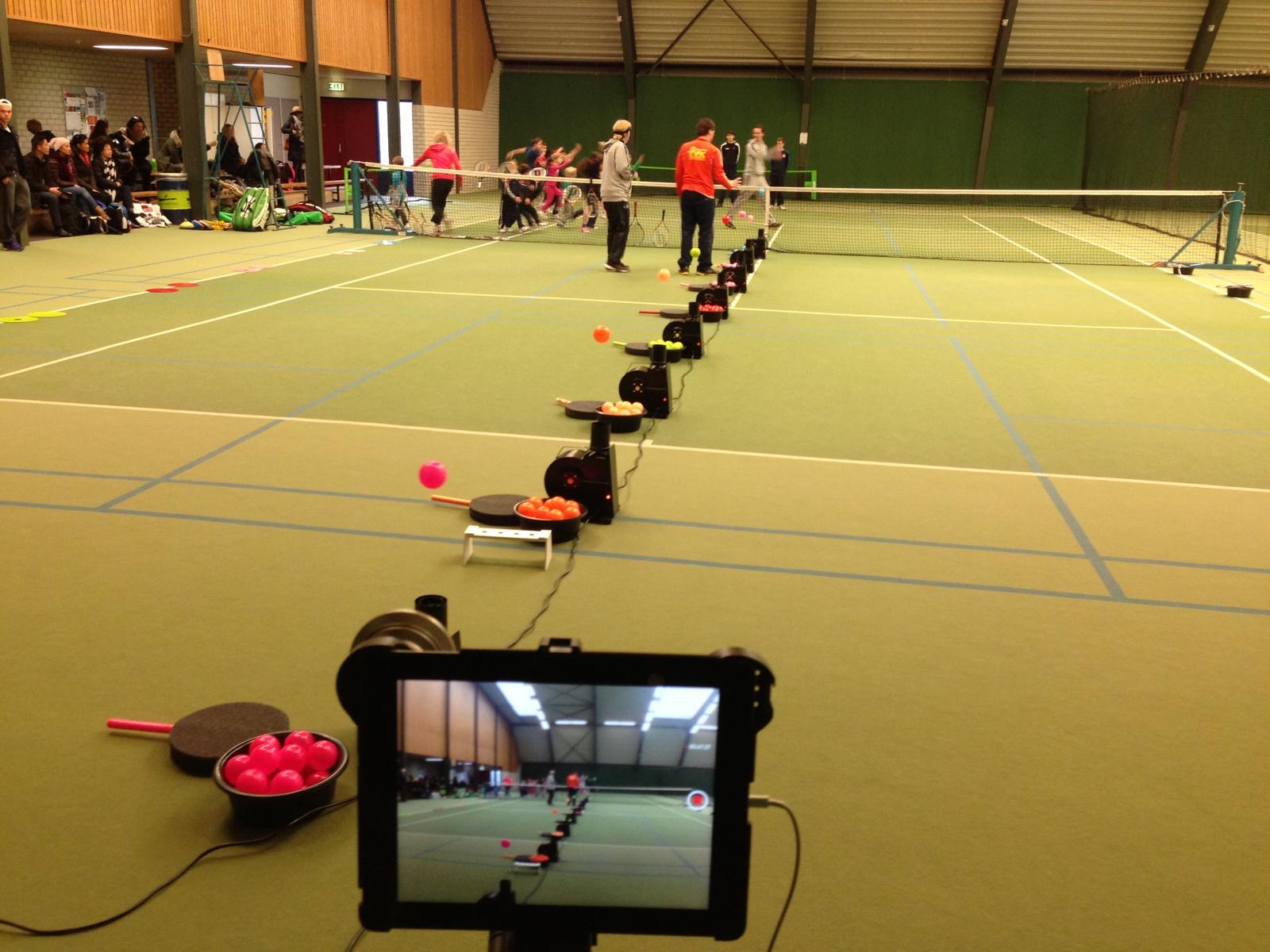 Row of floater machines with floating balls set up along the net in an indoor tennis hall