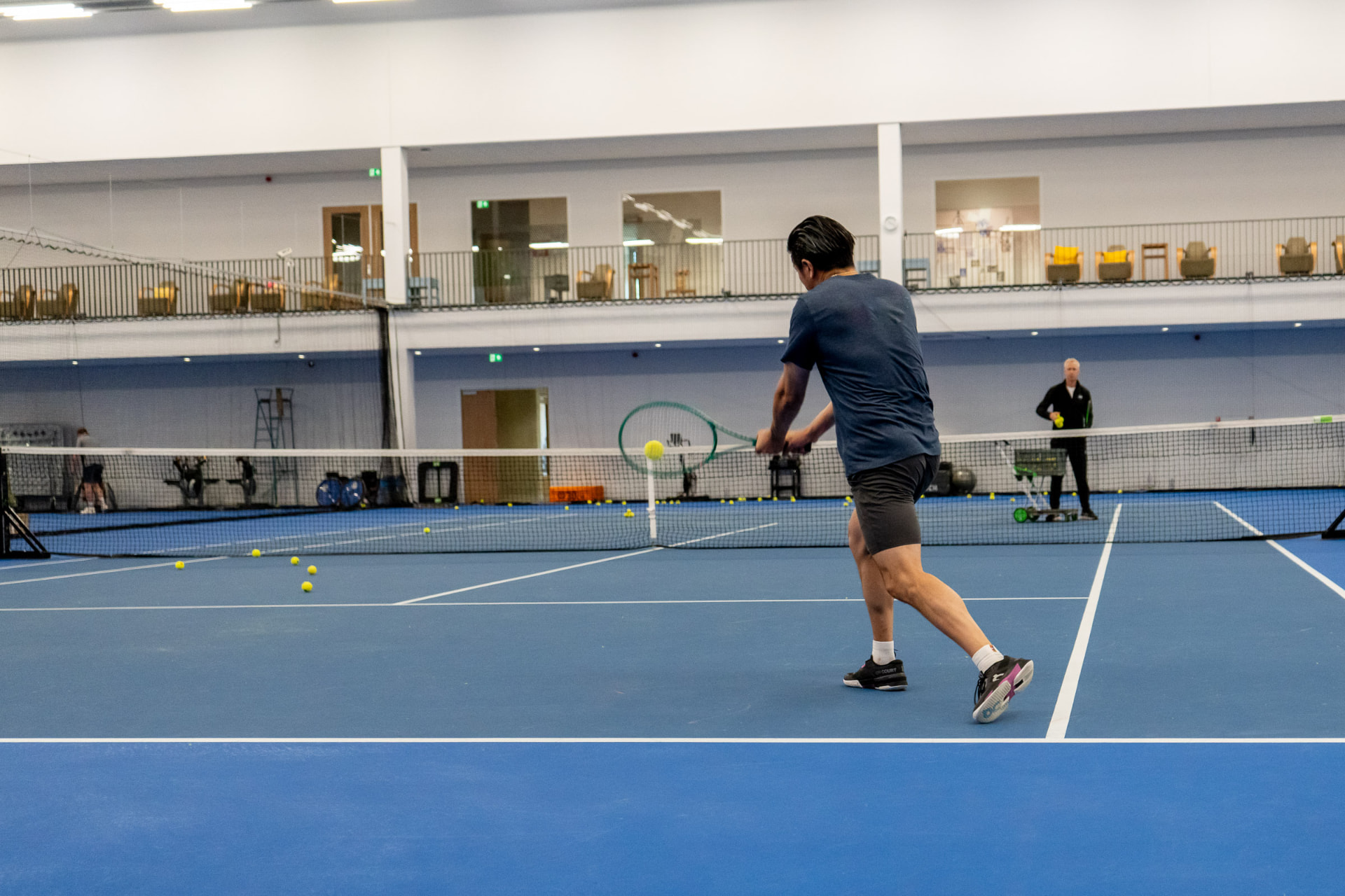 Adult player hits a backhand during an indoor tennis lesson on a hard court at NTC Amstelveen — 359.tennis