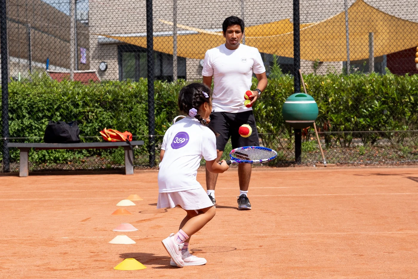 359-coach begeleidt een jong Tenniskids-lid in een persoonlijke duo-privéles op de gravelbaan